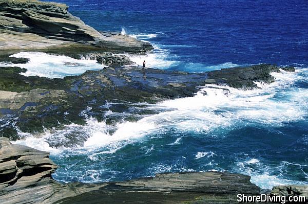 The entry is just about 30 feet to the right of where the man is standing off of a little platform into forty feet of water.  Giant Stride off the ledge, and you'll settle to the bottom at the entrance to an underwater arch.  Start swimming to your right.